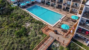 Vista aérea de un hotel con una gran piscina, zonas de estar al aire libre y una terraza con sombrillas.