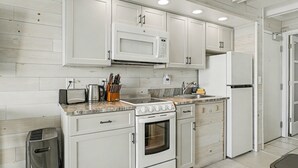 Una cocina moderna con armarios blancos, microondas integrado, estufa y refrigerador.