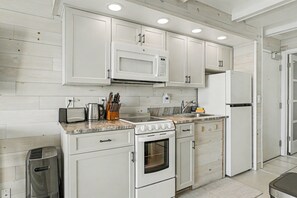 Una cocina moderna con armarios blancos, microondas integrado, estufa y refrigerador.