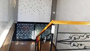 Un escalier avec une rampe en bois et des balustrades en métal noir, menant à une pièce dont un mur est recouvert de carreaux et qui possède une fenêtre ornée d’un motif floral.