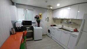 Une cuisine compacte avec des meubles blancs, un lave-linge, un four à micro-ondes et une petite table à manger avec des chaises.