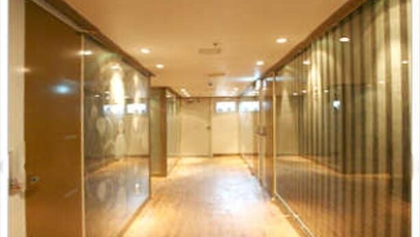 Un couloir doté d’un plancher en bois et de murs en verre, qui mène à une porte au bout.