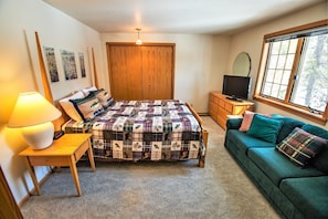 Un dormitorio con una cama, televisión, sofá, lámpara y ventana.