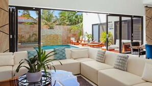 A modern living room with a large sectional sofa, a coffee table, and a view of an outdoor swimming pool area. - NEW LUX 5 Bed 5 Bath Pool Near To Beach By Bocobay (Noord)