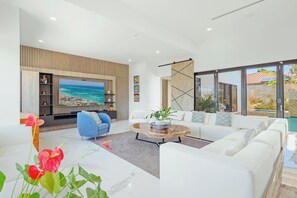 Una sala de estar moderna con un televisor grande, sofás blancos, un sillón azul y una mesa de centro.