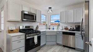 A modern kitchen with white cabinetry, stainless steel appliances, and a wooden floor. - Texas Getaway w/ Fire Pit, Grill & Ping-Pong (Leander)