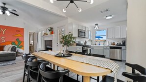 A modern kitchen with white cabinets, a microwave, and a stove. There is a dining area with a wooden table and black chairs. - Texas Getaway w/ Fire Pit, Grill & Ping-Pong (Leander)