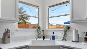 A modern kitchen with a central sink, two windows, and a view of a backyard. - Texas Getaway w/ Fire Pit, Grill & Ping-Pong (Leander)
