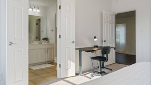 Une chambre à coucher avec un lit, un bureau avec une chaise et une salle de bain avec un lavabo et un miroir.