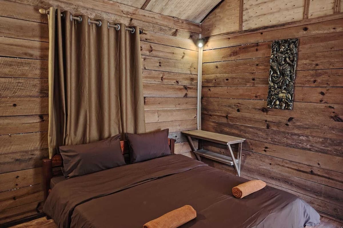 A wooden cabin room with a bed, curtains, a nightstand, and a wall decoration.