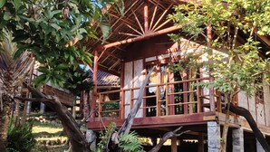 A wooden house with a thatched roof, built on stilts, surrounded by lush greenery. - Nirvana Archipel Resort (Vang Vieng)
