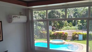 Habitación de hotel con cama, sofá gris, ventana con vistas a una piscina y jardín.