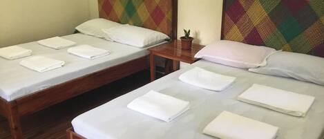Two single beds with wooden frames and white linens, a small table with a potted plant, and a colorful headboard.