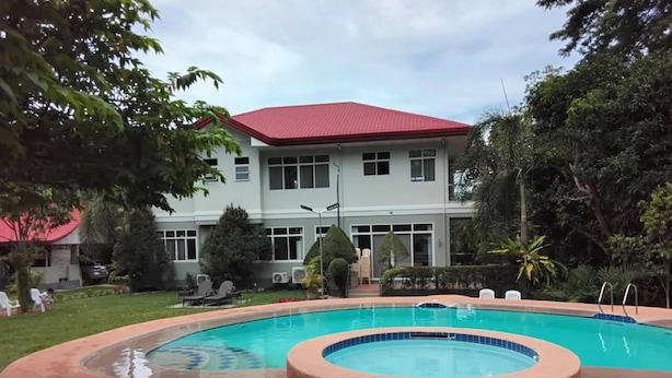 A swimming pool with a circular hot tub, surrounded by a landscaped garden and a building with a red roof in the background. - Room-camiguin Lanzones Resort Family roo (Mambajao)