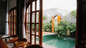 Zona de piscina con sillas de madera, pared de piedra y vistas al entorno verde.