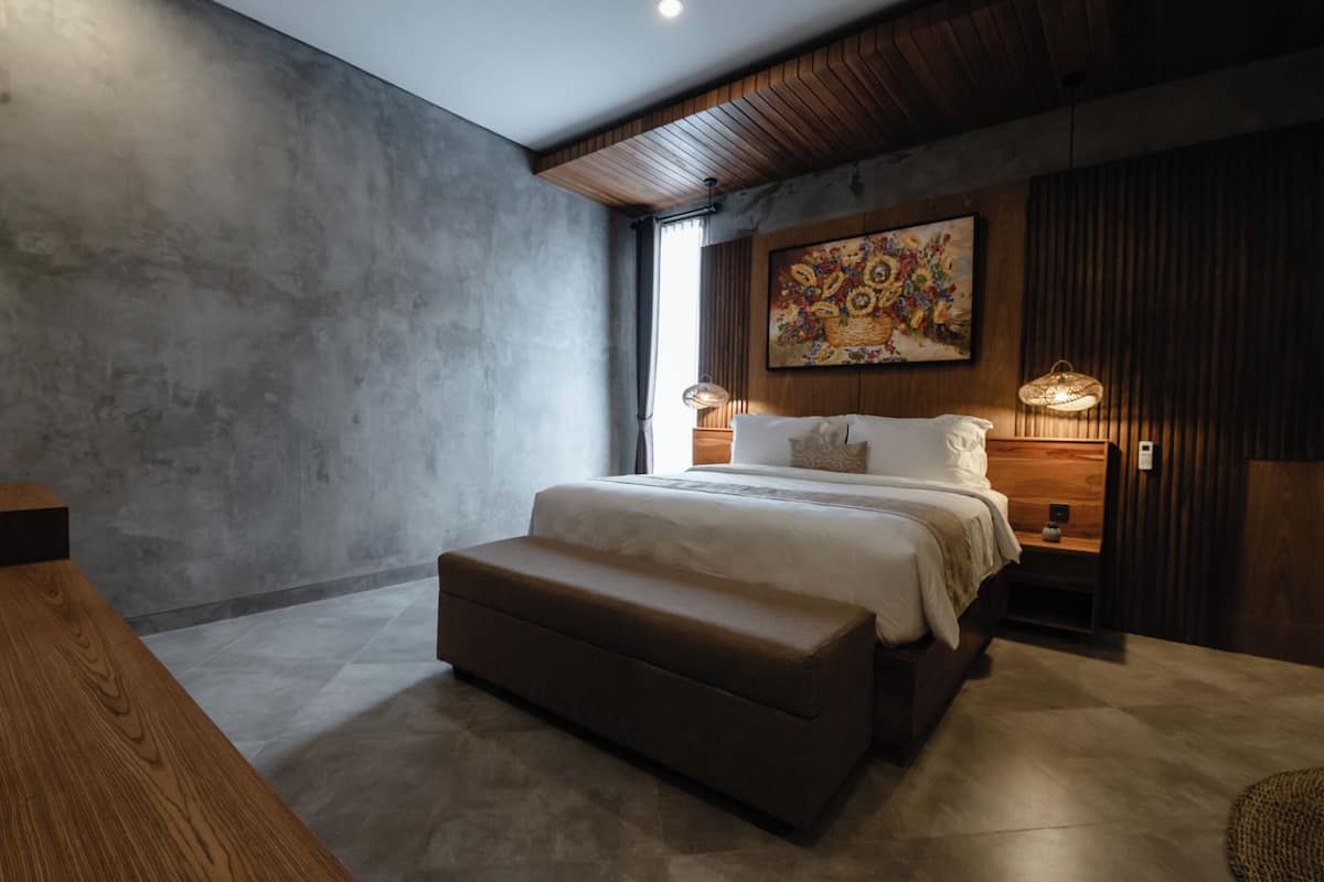 Un dormitorio moderno con una cama grande, un banco de madera, un cuadro y una lámpara.