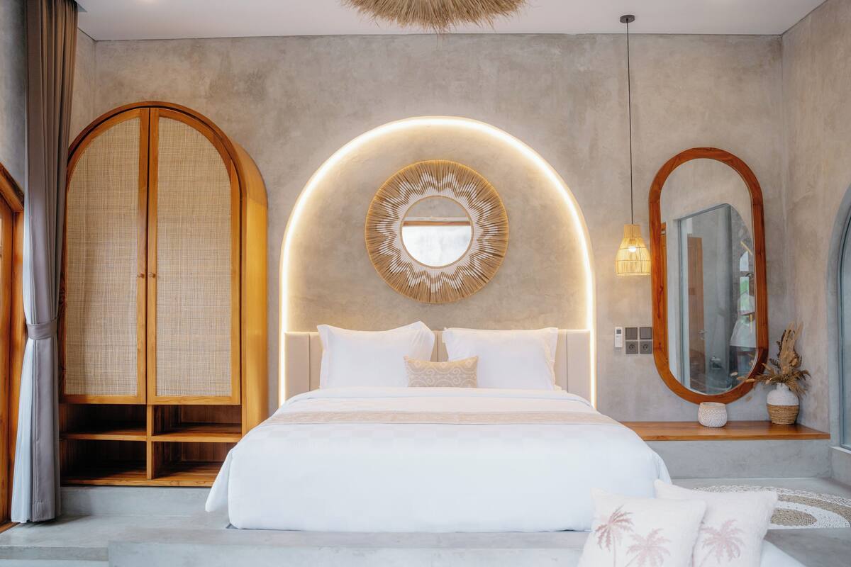 Un dormitorio moderno con una cama grande, un espejo redondo y un armario de madera.