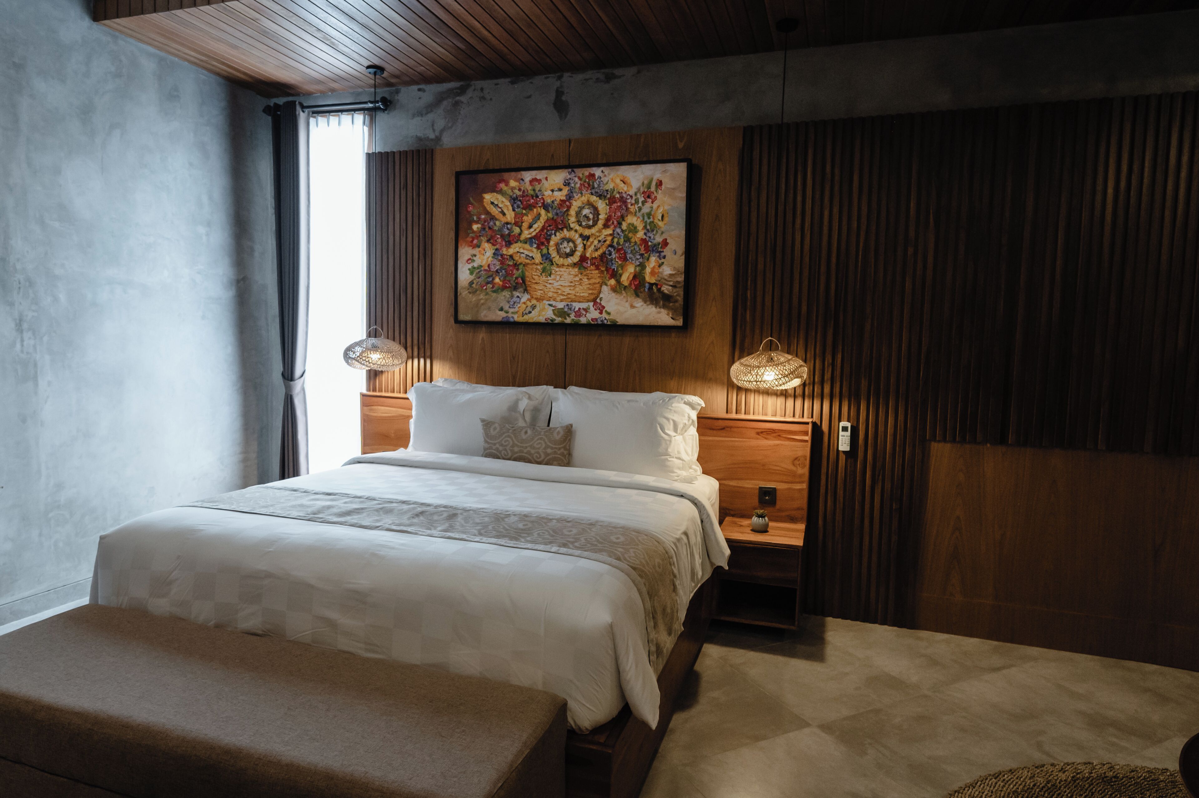 A bedroom with a large bed, a wooden headboard, a painting above the bed, and a nightstand with a lamp.