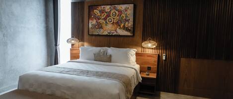 A bedroom with a large bed, a wooden headboard, a painting above the bed, and a nightstand with a lamp.