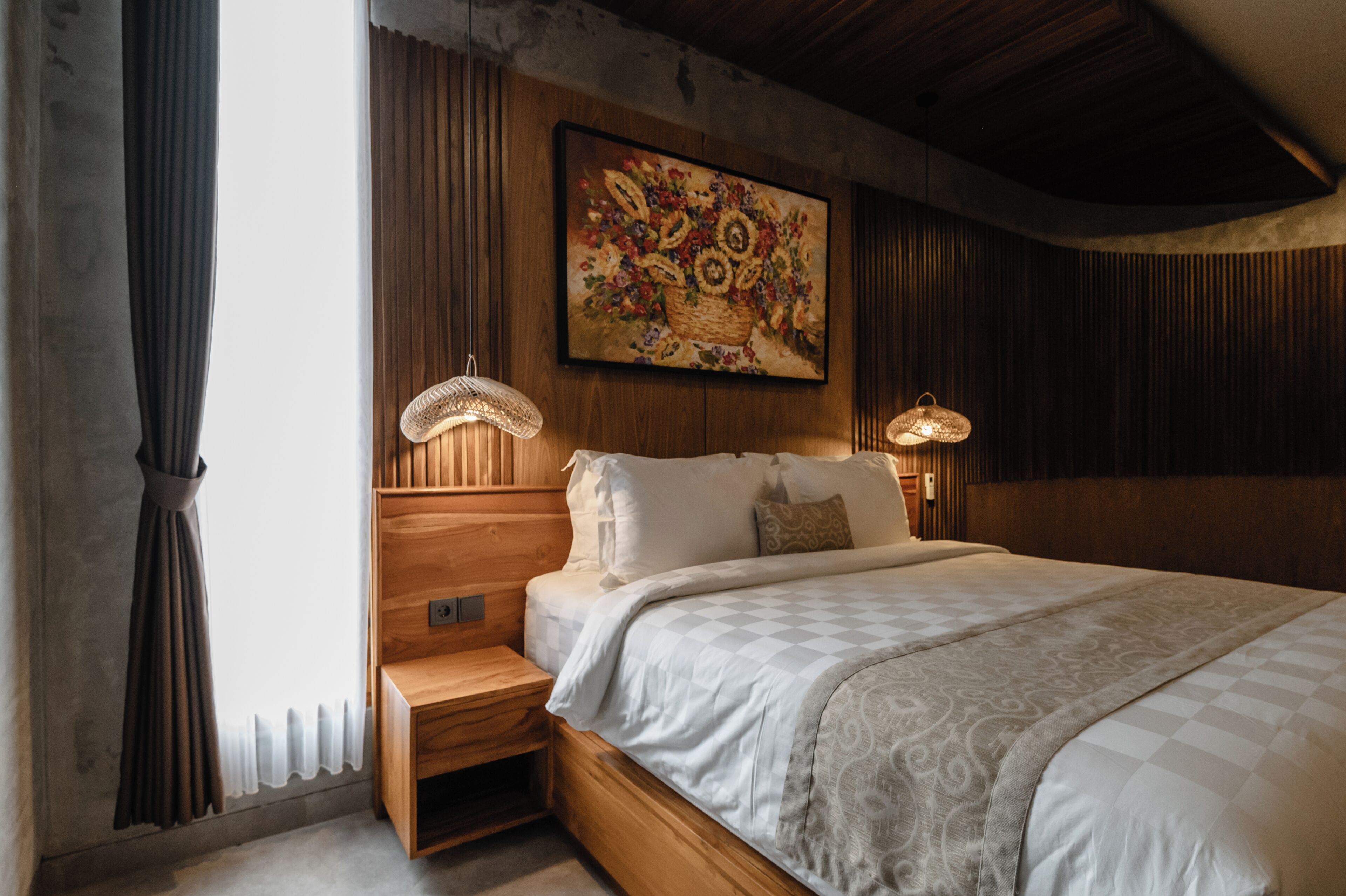 A bedroom with a wooden headboard, a large painting, two bedside lamps, and a bed with a patterned bedspread.