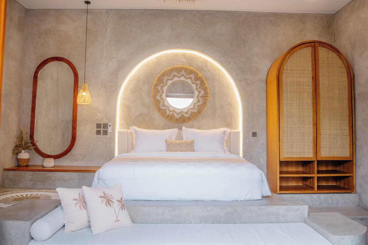 Un dormitorio moderno con una cama grande, un espejo redondo y un armario de madera.