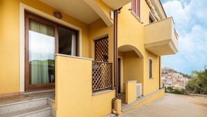 A yellow building with a balcony, steps leading to the entrance, and a view of a hillside town. - Apartment With air Conditioning and sea Views (Castelsardo)