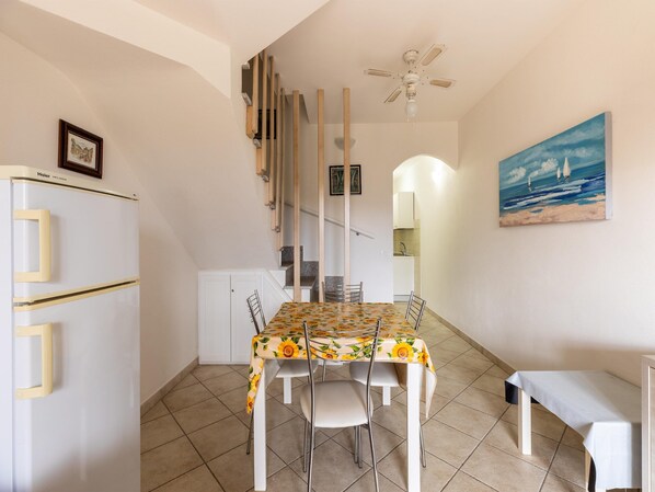 A compact kitchen with a dining table, chairs, a refrigerator, and a ceiling fan. - Apartment With air Conditioning and sea Views (Castelsardo)