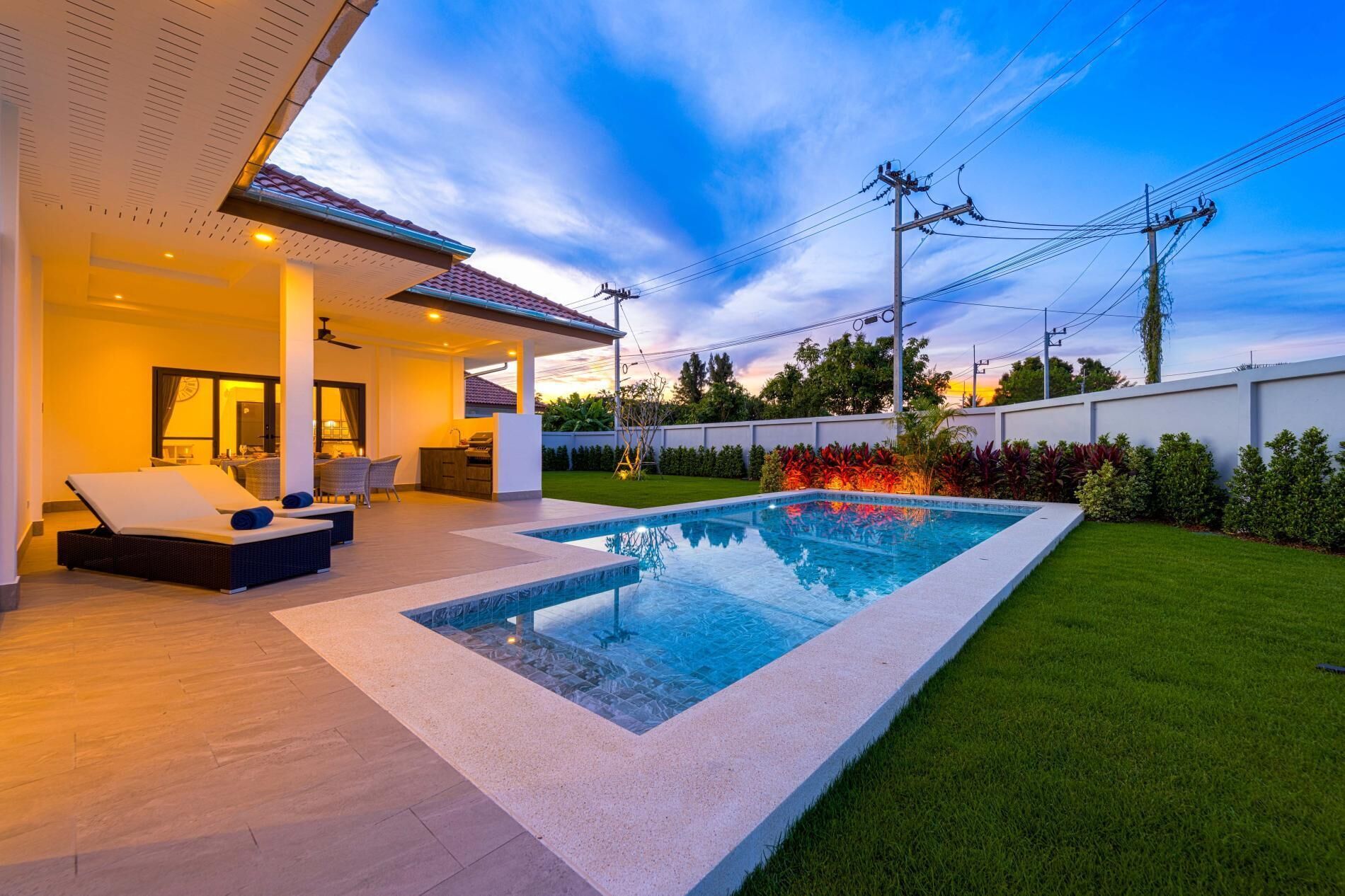 Un área de piscina exterior moderna con una tumbona y una zona de barbacoa.