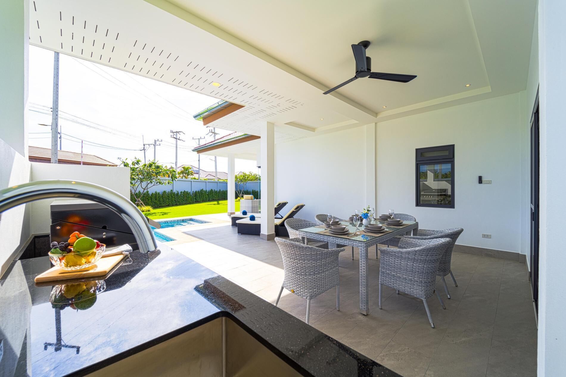 A modern outdoor dining area with a pool, a ceiling fan, and a view of the surrounding landscape.
