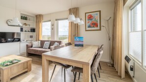Ett modernt vardagsrum med ett matbord i trä, en soffa och ett köksområde med en tv.