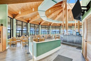 A spacious indoor area with wooden ceiling beams, large windows offering views of the outdoors, and a counter with seating. - Edgewater Resort!  2BR Sleeps 9!  1st Floor Condo (Panama City Beach)