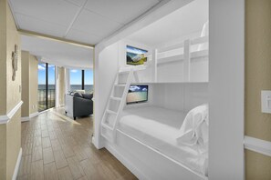 A bedroom with a bunk bed, a TV, and a balcony with a view of the ocean. - Edgewater Resort!  2BR Sleeps 9!  1st Floor Condo (Panama City Beach)