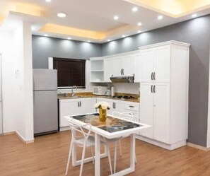 A compact kitchen with white cabinetry, a dining table with chairs, and a refrigerator.
