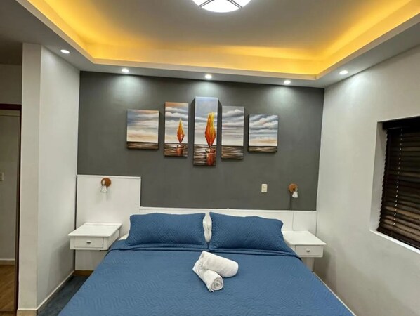 Un dormitori amb un llit, dues taules de nit i una paret amb quatre quadres.