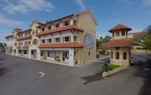 A multi-story hotel with a central courtyard, featuring a large circular sign, and a smaller structure with a red-tiled roof.