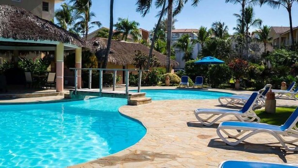 Uma piscina com espreguiçadeiras e uma cobertura de palha.