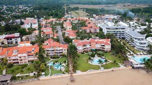 Resort com vários edifícios, praia e montanhas ao fundo.