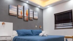 Quarto com cama, mesa de cabeceira, luminária na parede e janela com persianas.