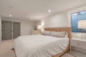 Ein Schlafzimmer mit einem großen Bett, einem Nachttisch, einer Lampe und einem Fenster mit Blick.