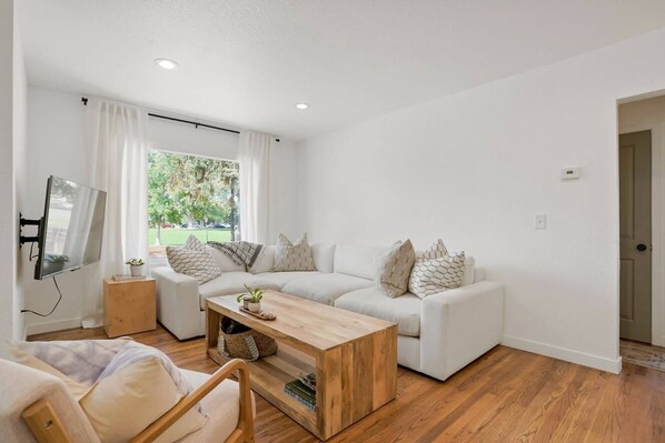 Ein modernes Wohnzimmer mit einem weißen Sofa, einem Holztisch und einem Fernseher auf einem Standfuß.