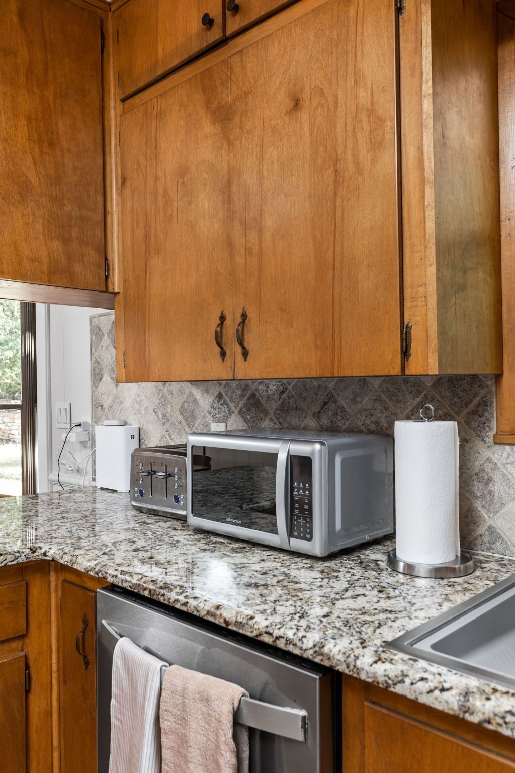 A kitchen with wooden cabinets, a granite countertop, a toaster, a microwave, and a dishwasher.