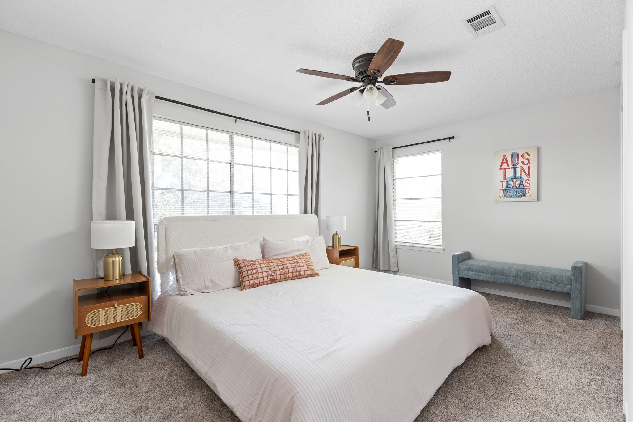 A bedroom with a bed, bedside tables, a ceiling fan, and a window with curtains.