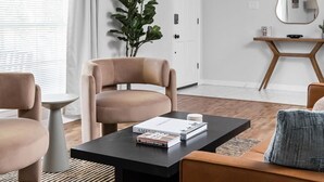 En moderne stue med sofa, lænestol og sofabord. Der er en plante, et spejl og en dør i baggrunden.