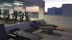 Une salle de sport équipée de matériel d’exercice, dotée d’un grand miroir et de fauteuils confortables sur une terrasse sur le toit.