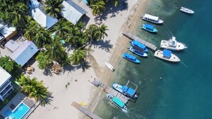An aerial view of a beachside resort with multiple boats docked, a swimming pool, and a wooden pier.