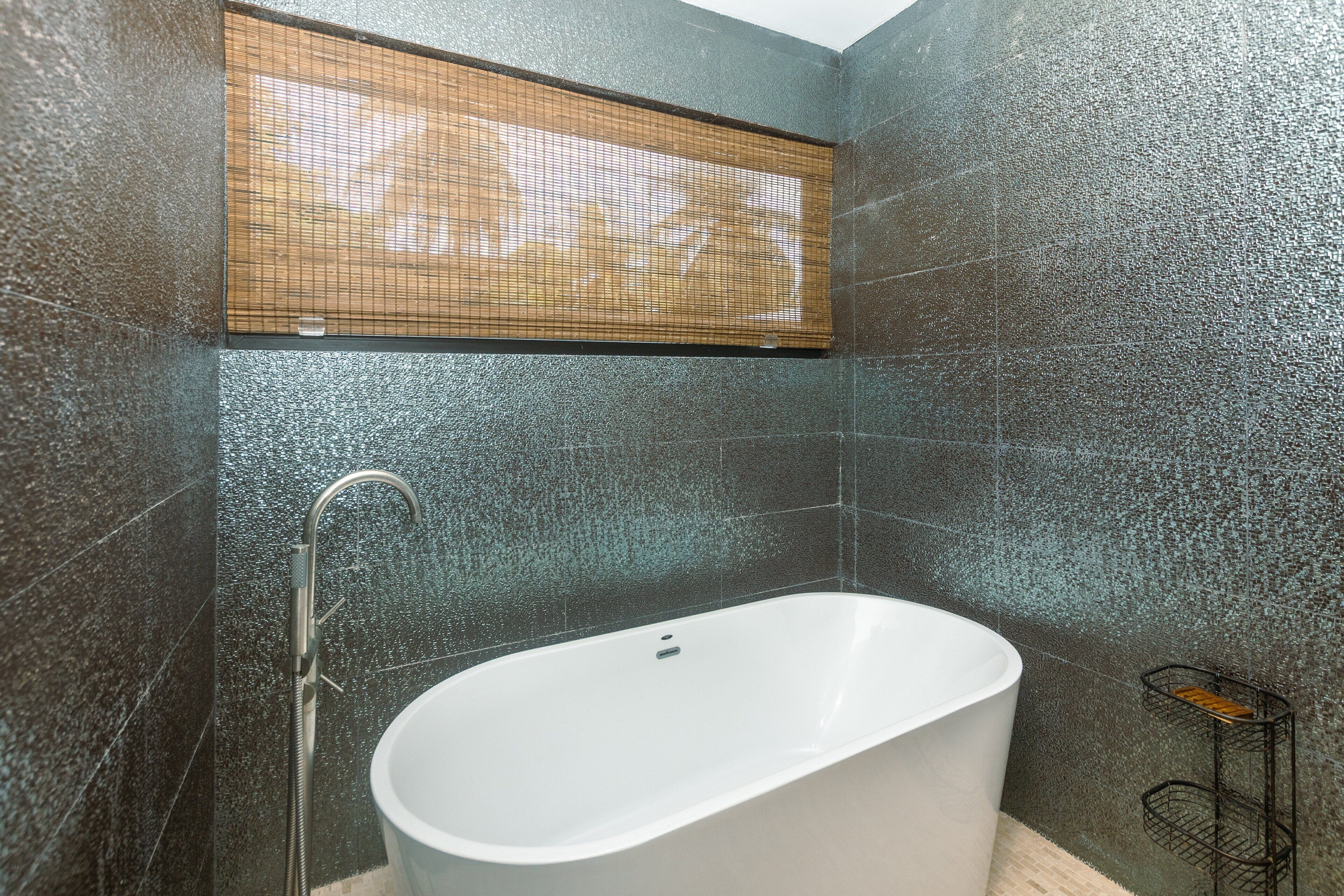 Een moderne badkamer met een vrijstaand bad, een douchekop en een bamboe zonnescherm voor het raam.