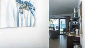 A modern kitchen with a view of the sea, a dining area, and a large painting of a sea turtle.