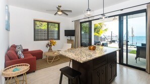 A modern kitchen with a central island, a red sofa, and a dining area with a view of the ocean.
