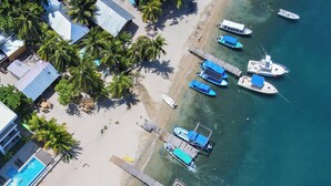 Una vista aerea di un resort sulla spiaggia, con diverse imbarcazioni ormeggiate, una piscina e un molo di legno.
