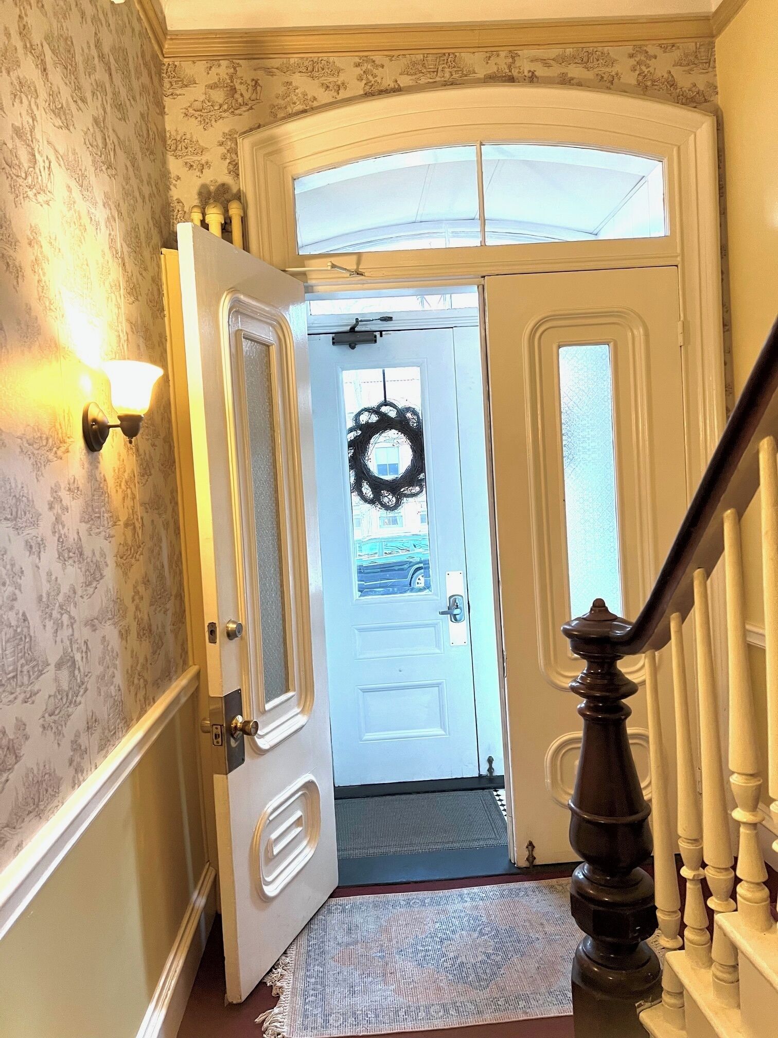 Un couloir avec une porte blanche, une couronne noire et un luminaire fixé au mur.